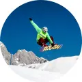 Kulatý jedlý obrázek na dort – Snowboard, jezdec v zelené bundě ve vzduchu (modrá, bílá, zelená)